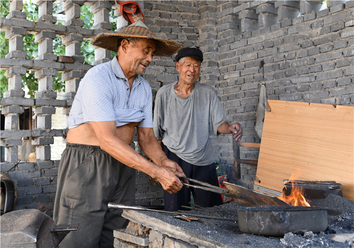铁匠兄弟贾兹云和贾兹远在火炉旁,一人拉风箱,一人持火钳.